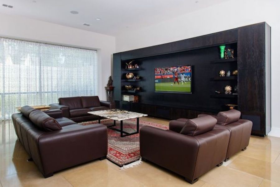 Home media room with dark feature wall and big screen television, large picture windows with curtains, and brown leather couches.