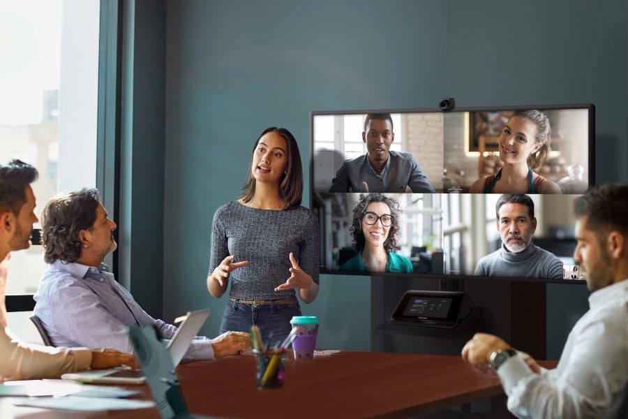 A video conference meeting using Crestron Flex with four people viewed on the display and four in the meeting room.