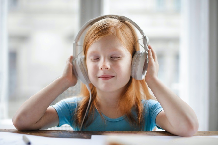 Little girl sitting at the kitchen table with headphones on, her eyes closed, smiling.