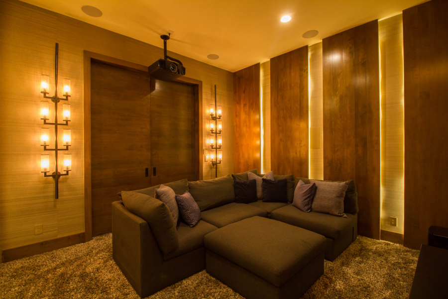 home theater space with sectional seating, yellow-toned lights, and a projector hanging from ceiling